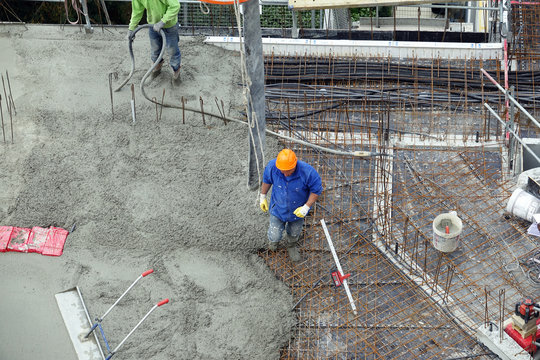 Des ouvriers en ma&ccedil;onnerie s'affairant sur une dalle de b&eacute;ton d'un immeuble en construction