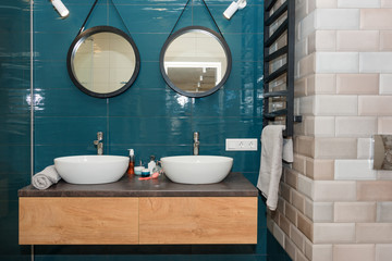 Fototapeta na wymiar Modern bathroom interior with a wooden shelf, two sinks standing on it and round mirrors. Transparent glass shower cabin, minimalist scandinavian bathroom in loft apartment