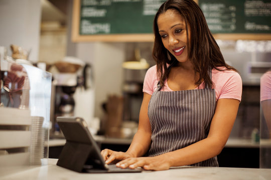 Low angle view of smiling female owner using tablet computer on bar counter while standing in coffee shop