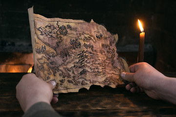 Adventurer man is holding in hands a treasure map over a burning fire background. Treasure hunt...