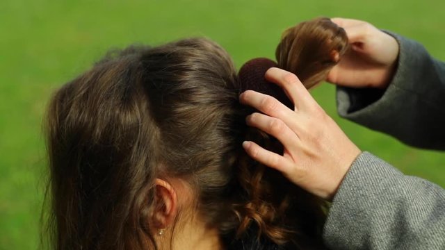 Stylist applying a circle to her hair and preparing a braid for a model with long brown hair outside during a sunny day