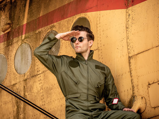 A handsome young pilot sitting on the wing of a plane and covering the sun