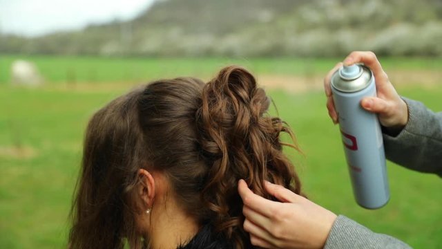 Stylist applying hardener to model with long brown hair outdoors during sunny day