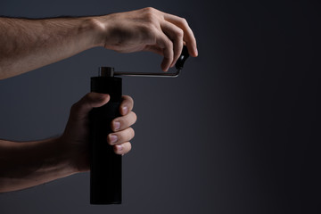 Fototapeta premium A man grinds grain coffee with a manual coffee grinder. Dark background