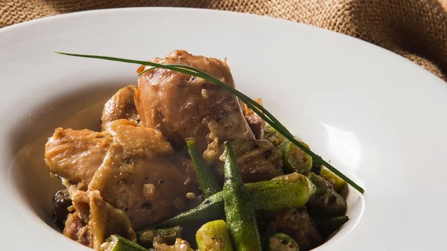 Slide shot Frango com quiabo (Portuguese for "chicken with okra"), Brazilian dish in white plate with smoke.