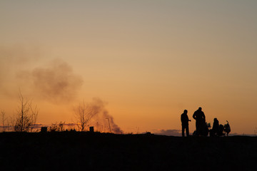 Naklejka premium The main theme of this picture is the shadow and the silhouettes of people against the backdrop of the sunset. Sunset on the bay. People relax, walk. Family roasts meat.