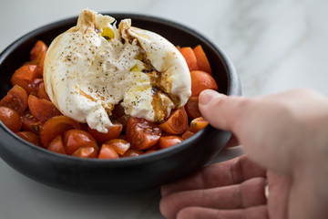 Frau isst Burrata Büffelmozzarella Kugel mit Tomaten, Olivenöl und Balsamico auf schwarzen Teller