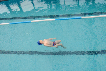 top view of a 7-year boy swimming backstroke in a swimming pool