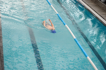 top view of a 7-year boy swimming backstroke in a swimming pool