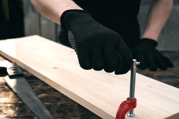 Worker secures a wooden board on a workbench with a clamp.