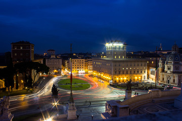Square in the center of Rome in Italy at night with colorful cars tracks, trails. Long exposure image. Historical and residential buildings on the background and statue of palace on the foreground.