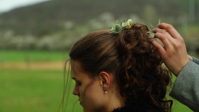 Preparing the bride's hair entangling flowers into long brown hair in a braid