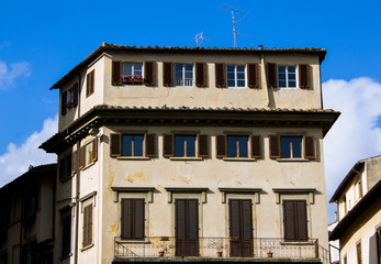 Fototapeta na wymiar Facade of residential Italian building with shutter windows and balconies on it and blue bright sky above. Florence, Firenze building, street near the center of Florence. Touristic street.