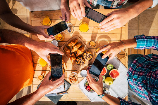Morning breakfast table full of coffee and food viewed from top vertical above with group of people enjoying and taking pictures with mobile phones together to share on internet. Colorful background