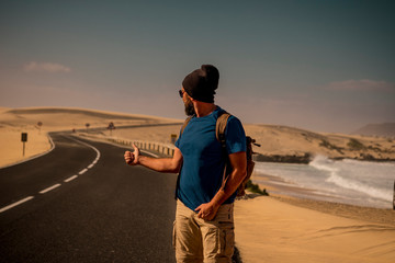 Hitcher people caucasian man  for people travel concept with backpack in outdoor scenic dersrt sand beach place - traveler lifestyle adult male with long asphalt road in background