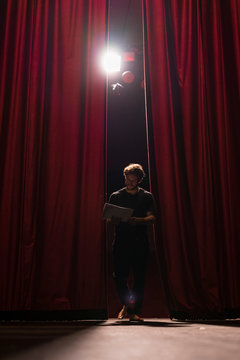 Barefoot actor walking on stage of theatre studying script