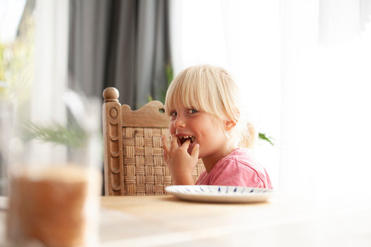 Portrait of tricky little girl sitting at dining table eating