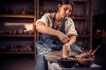 Beautiful ceramist sculptor works with clay on a Potter's wheel and at the table with the tools....