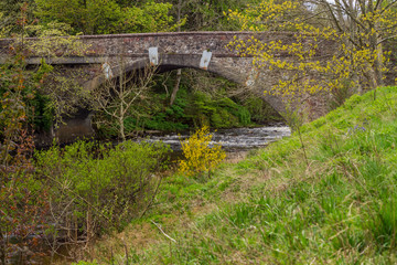 Old stone bridge over a river running through verdant countryside.