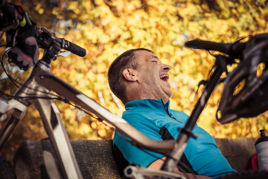 Laughing man with mountain bike having a break sitting on a bench