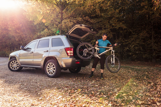 Man on forest car park unloading mountain bike from car