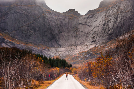 Norway, Lofoten Islands, man standing on empty road surrounded by rock face