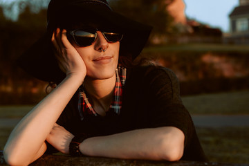 Pensive woman wearing trendy sunglasses with black hat leaning on hand and looking away in sunlight