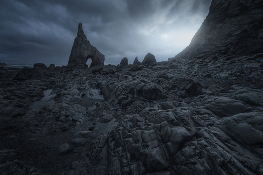 Picturesque view of stony shore with sharp crag on background of gloomy cloudy sky