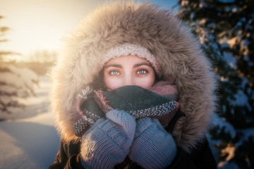 Young attractive female in warm clothing with fur joyful laughing beside covered snow conifer tree
