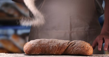 In the bakery, a baker after baking fresh bread sprinkles sugar powder (flour) on bread (flour pastry) with a powder colander (with hands). Concept of: Fresh bread, Home-made, The hands, Slow Motion.