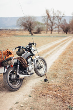 Fishing pole and motorcycle located on narrow countryside road in dry field during trip in nature