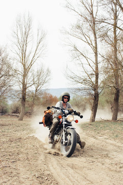 Male in helmet riding fast motorbike on dusty countryside road near leafless trees in nature