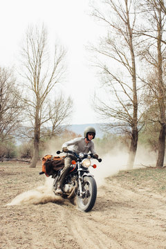 Male in helmet riding fast motorbike on dusty countryside road near leafless trees in nature