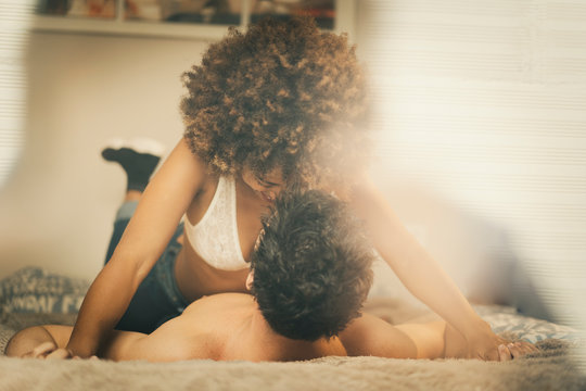 Young diverse man and woman lying on bed and cuddling in cozy room at home