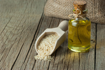 Glass bottle of sesame oil and raw sesame seeds in wooden shovel on wooden table. Uncooked sesame...