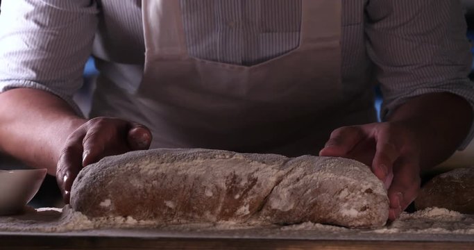 In the bakery, a baker blows off flour from bread, a lot of flour in the air. Concept of: Dirty hands, Flour, Chef, Baker.