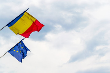 Romanian flag and European Union flag waving in high winds, with stormy clouds in the background, in Sibiu, Romania - copy space on the right. Politics, business cooperation, EU summit.