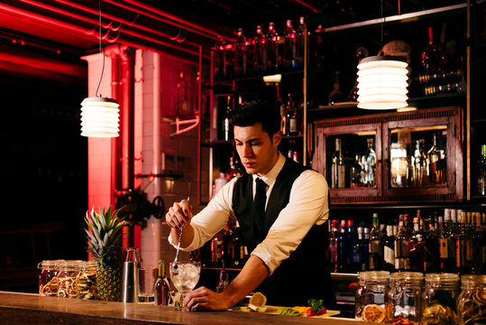 Young elegant barman working behind a bar counter mixing drinks with fruits