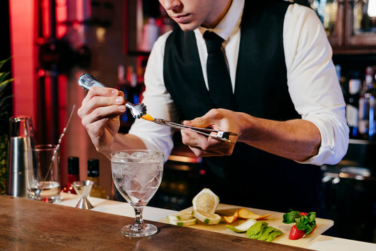 Crop anonymous young elegant barman working behind a bar counter mixing drinks with fruits