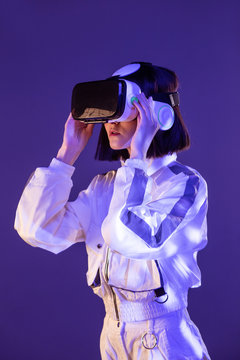 Excited young woman having virtual reality experience in neon light