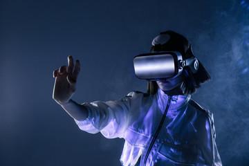 Excited young woman touching air while having virtual reality experience in neon light