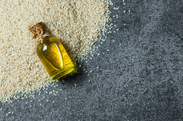 Glass bottle of sesame oil and raw sesame seeds on grey rustic table. Uncooked sesame background...