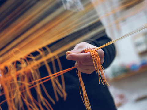 Crop person holding threads on loom