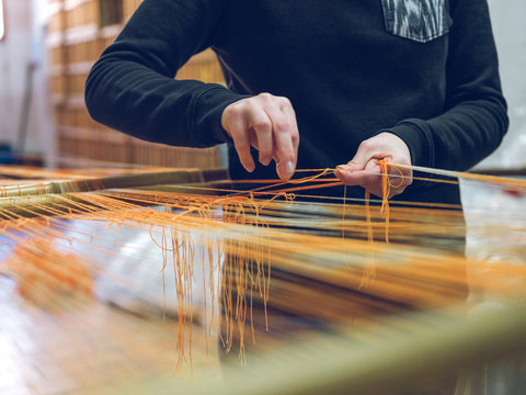 Crop person holding threads on loom