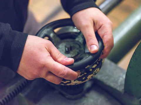 Hands of anonymous worker turning rusty valve on metal industrial machine on factory
