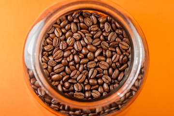 Fresh and ground roasted coffee beans from the coffee plant inside a cylindrical glass jar.