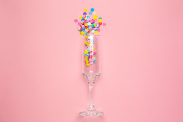 Champagne glass with multi-colored confetti on pink color paper background . Flat lay composition for birthday, mother day or wedding