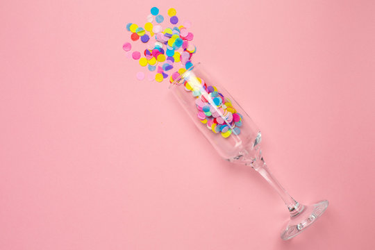 Champagne glass with multi-colored confetti on pink color paper background . Flat lay composition for birthday, mother day or wedding