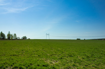 Fototapeta na wymiar Power line in the village. Green meadow and blue sky