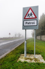 School Patrol sign beside a road with fog/mist/limited visibility